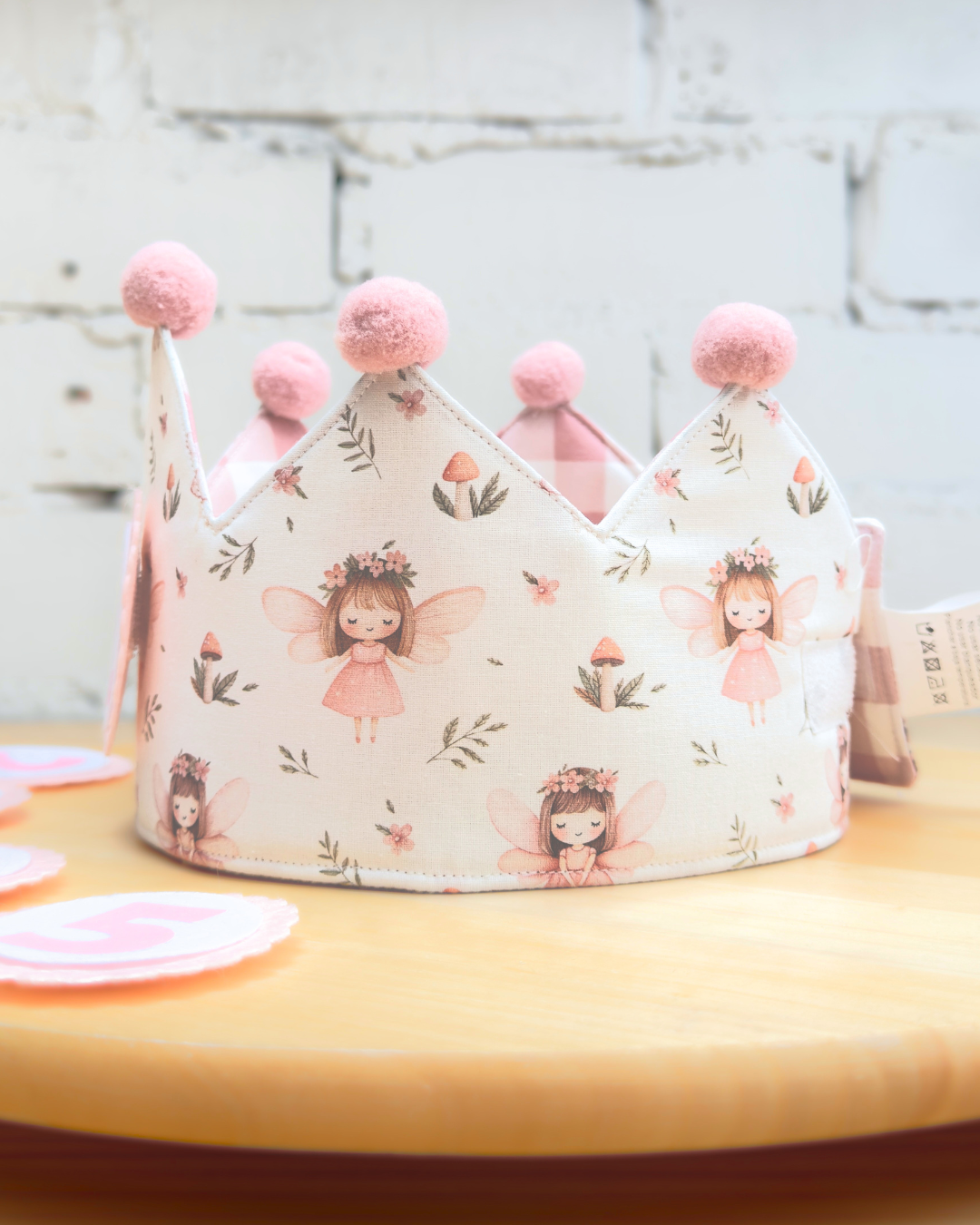 Detalle del estampado de hadas con flores sobre fondo crema y los pompones rosas