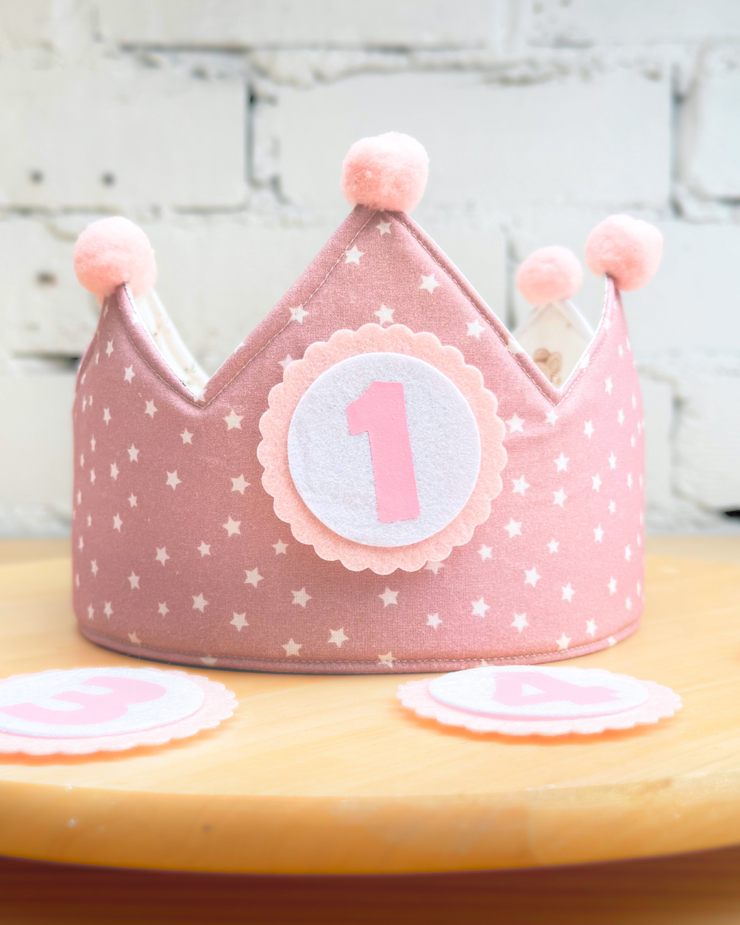 Cara reversible en rosa con estrellitas blancas, con pompones rosas y el número 1