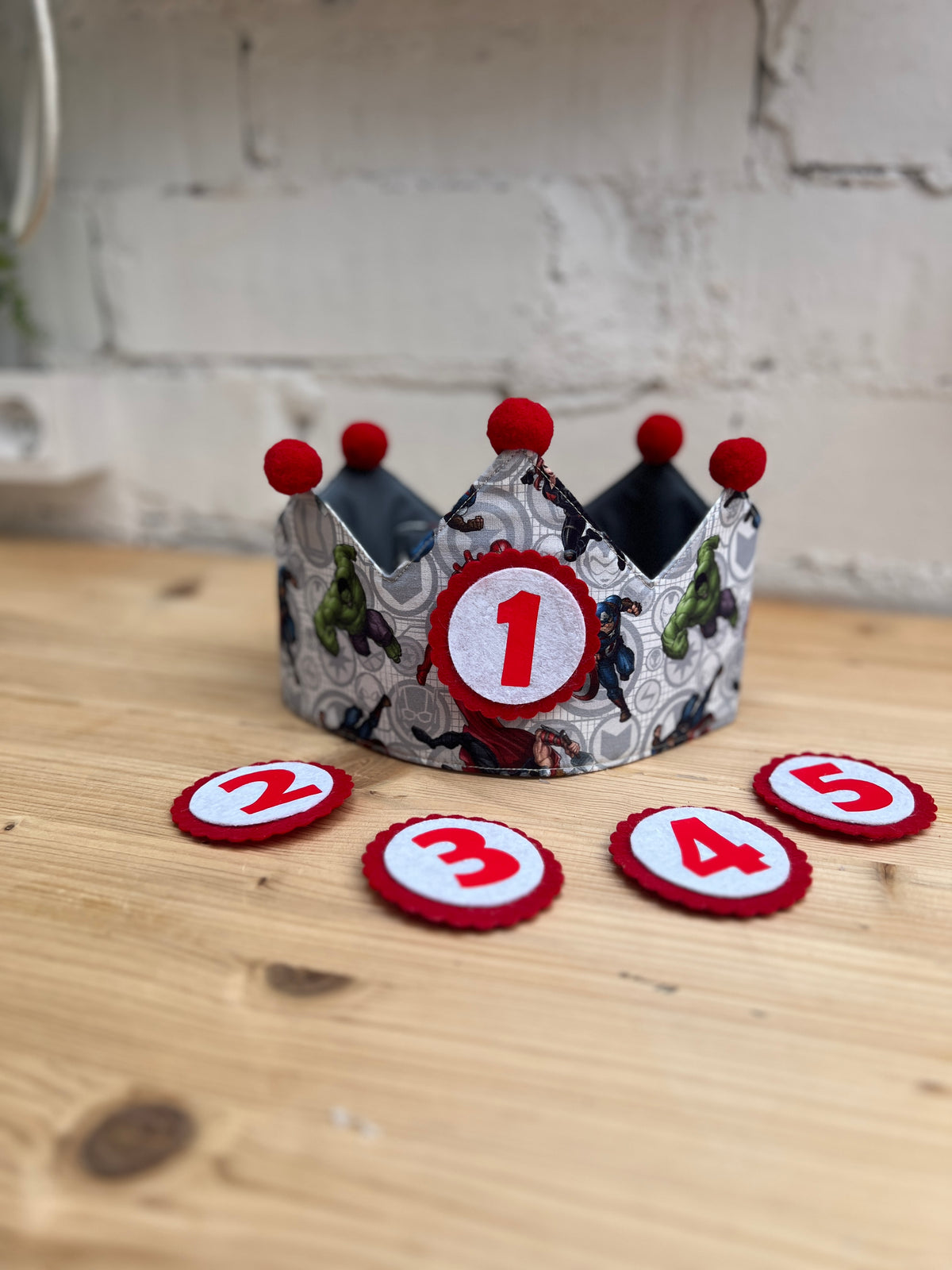 Corona de cumpleaños con estampado de superhéroes en gris y pompones rojos, con los números intercambiables del 1 al 5